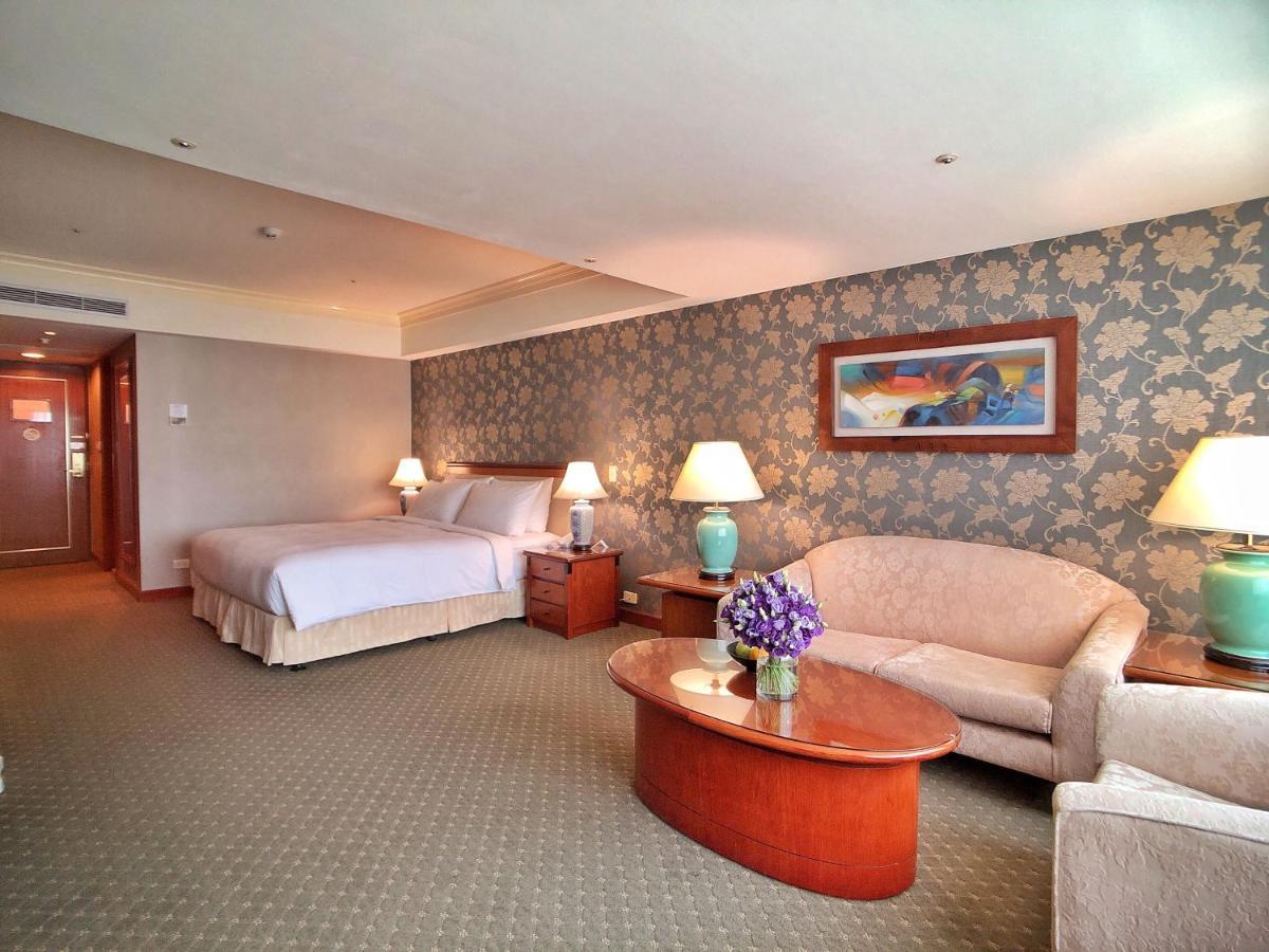 Evergreen Laurel Hotel - Taichung Luaran gambar The photo shows a hotel room that features a well-furnished space. It includes a large bed with a light-colored bedspread, a comfortable sofa, and armchair. There's a coffee table with a vase of flowers in the center. The room has a decorative wallpa
