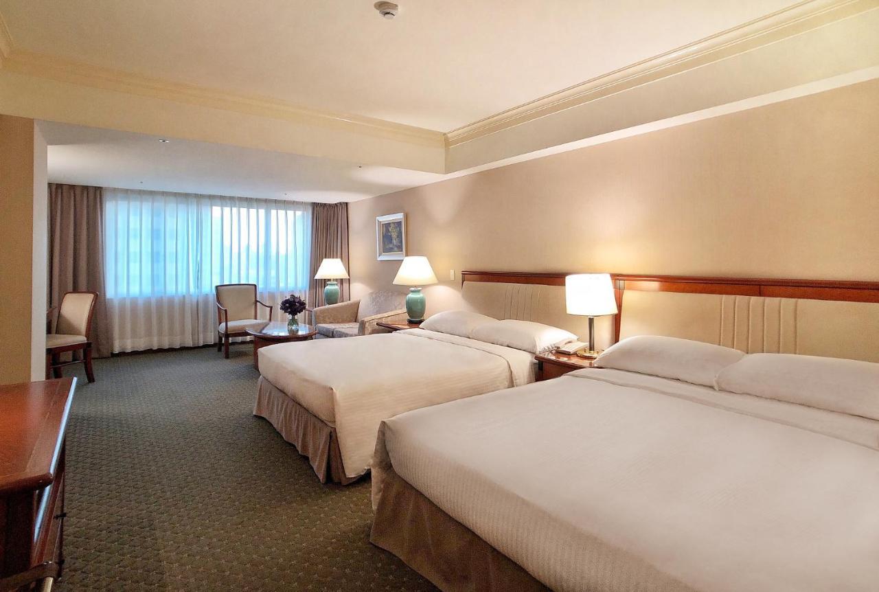 Evergreen Laurel Hotel - Taichung Luaran gambar The photo shows a hotel room featuring two queen-sized beds with white linens. The room is well-lit and has a warm, neutral color palette. There are bedside lamps on each side of the beds and a small table. To the side, there's a comfortable armchair