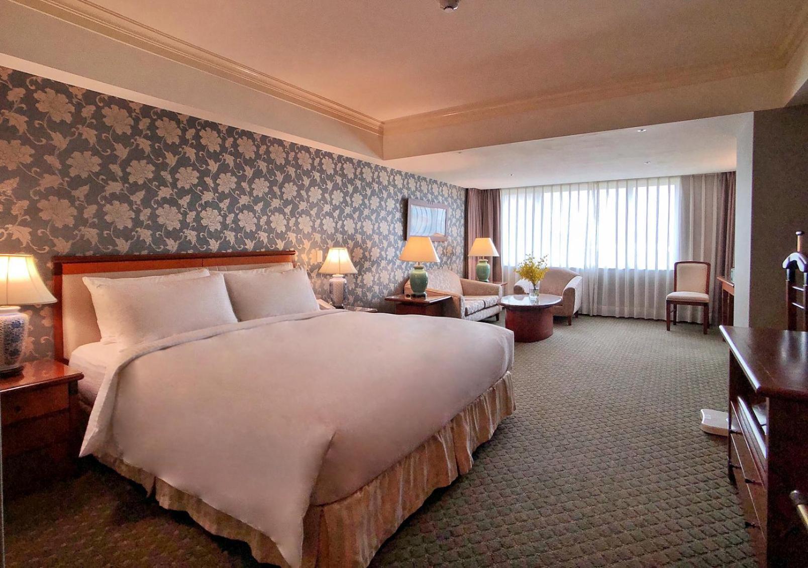 Evergreen Laurel Hotel - Taichung Luaran gambar The photo shows a hotel room with a spacious and comfortable layout. It features a large bed with white bedding, placed against a decorative wallpapered wall. On either side of the bed, there are lamps providing soft lighting. In addition to the bed,
