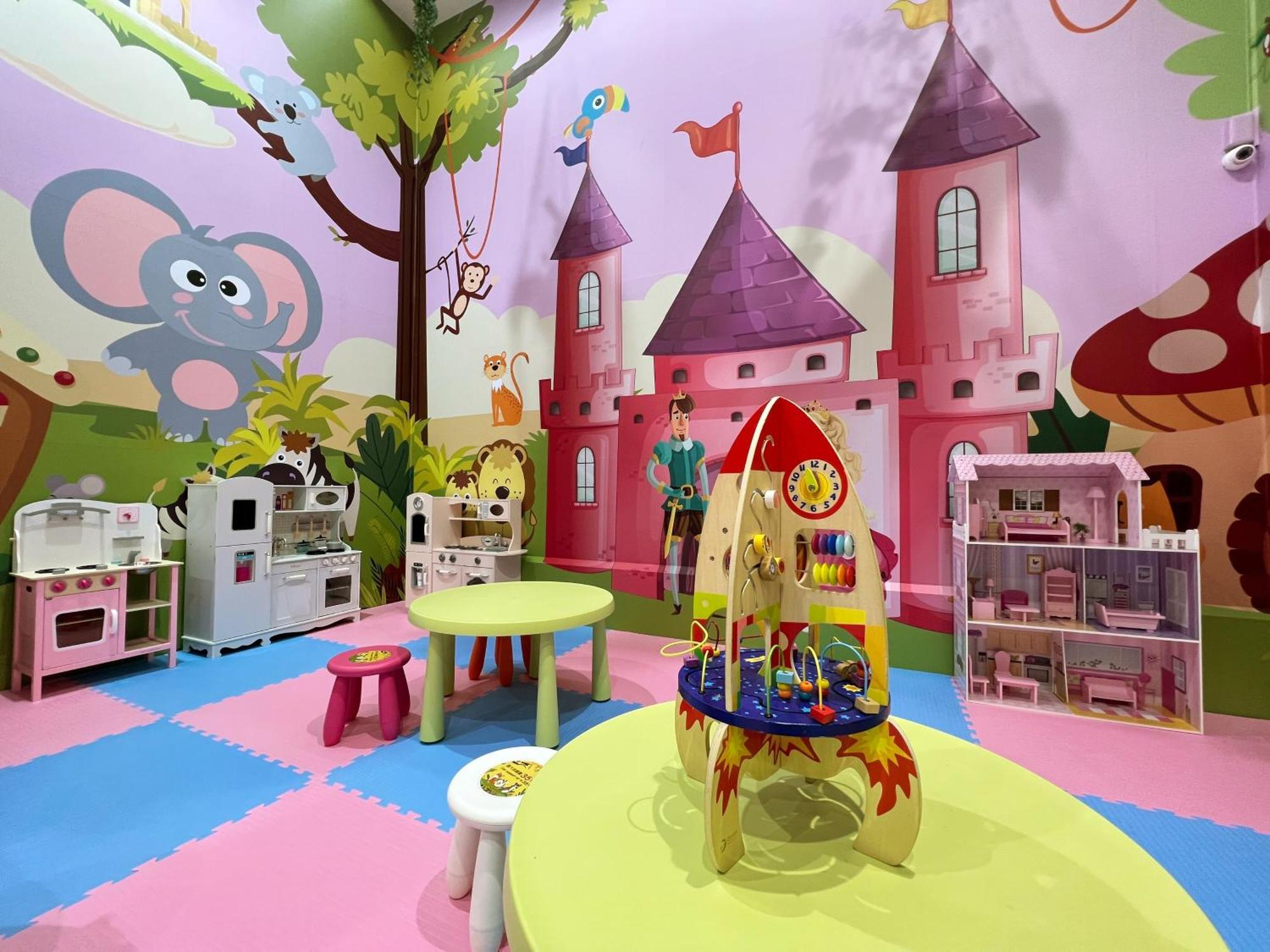 Evergreen Laurel Hotel - Taichung Luaran gambar The photo shows a colorful children's playroom designed with a whimsical theme. The walls are painted in bright colors and feature a cartoon-style mural of a pink castle with purple towers and a smiling cartoon elephant. The room is filled with playf