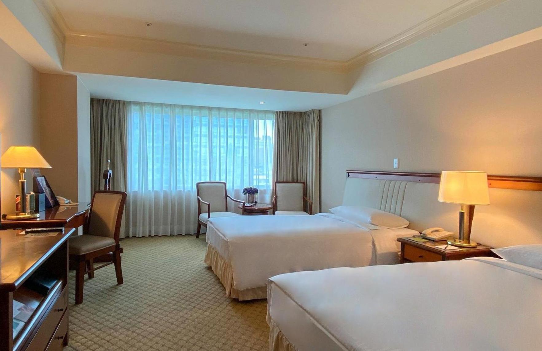 Evergreen Laurel Hotel - Taichung Luaran gambar The photo shows a hotel room featuring two single beds positioned near each other. There's a light-colored carpet on the floor and a large window with sheer curtains that allows natural light to fill the space. In the room, there are two chairs place