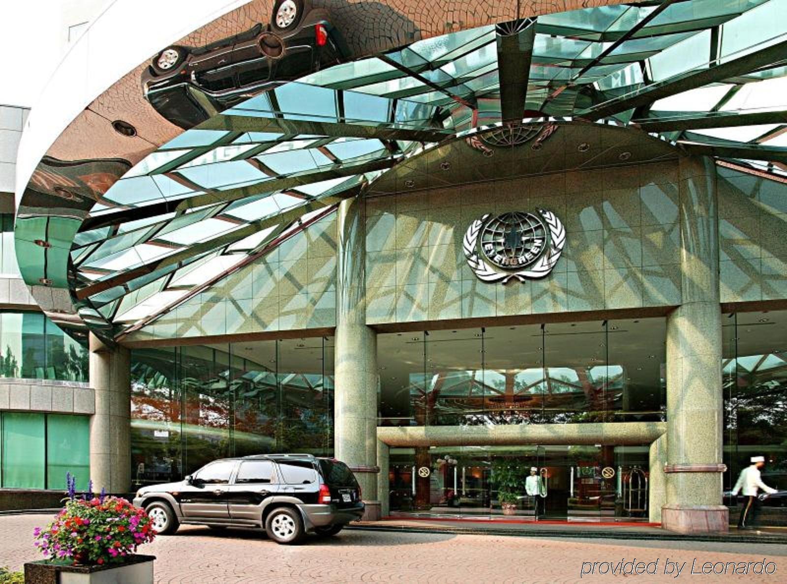 Evergreen Laurel Hotel - Taichung Luaran gambar The photo shows the entrance of a modern building characterized by its glass and metal architecture. The structure features a large, domed roof that reflects light, with a distinctive emblem or logo displayed prominently at the center. In front of th
