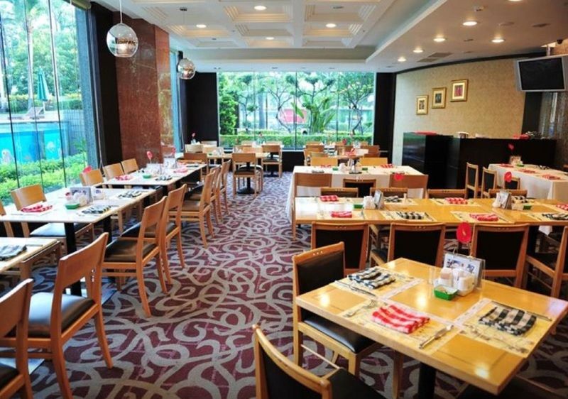 Evergreen Laurel Hotel - Taichung Luaran gambar The photo shows an interior of a restaurant with a spacious layout. There are several wooden tables, each set with napkins and utensils. The floor has a decorative carpet, and large windows provide a view of greenery outside. The lighting is bright, 