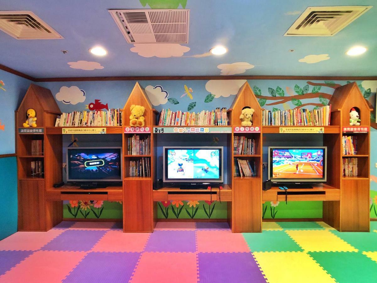 Evergreen Laurel Hotel - Taichung Luaran gambar The photo shows a colorful and playful room designed for children. In the center, there are three wooden gaming stations, each equipped with a television screen and surrounded by shelves filled with books. The walls are decorated with cheerful images