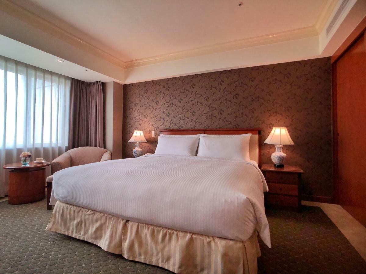 Evergreen Laurel Hotel - Taichung Luaran gambar The photo shows a neatly arranged hotel room featuring a large bed with white linens and a light-colored bed skirt. On either side of the bed, there are small wooden nightstands with lamps. To the left of the bed, there's a comfortable chair and a ro