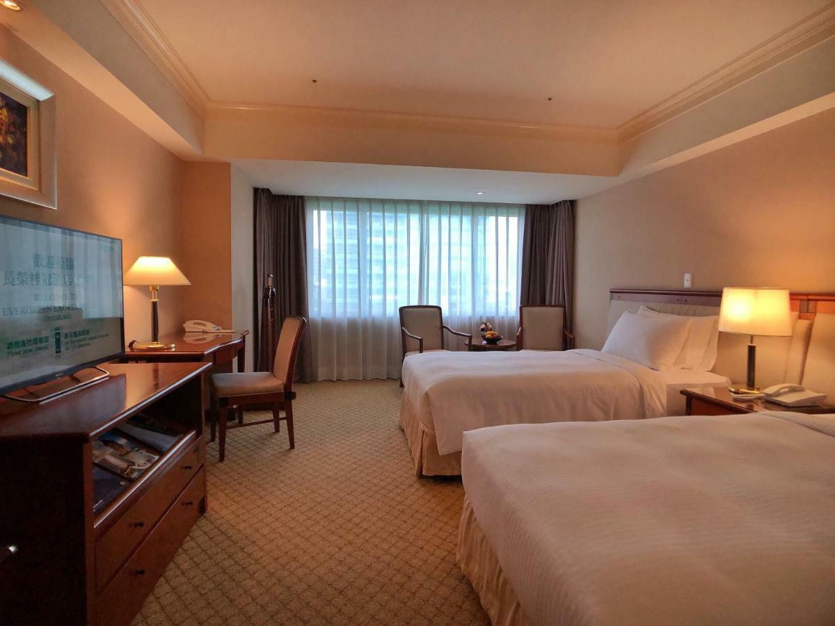 Evergreen Laurel Hotel - Taichung Luaran gambar The photo shows a hotel room featuring two twin beds with white bedding. There's a television mounted on a wooden dresser, and next to it, a comfortable chair and a small table are positioned. The room has large windows that allow natural light to en