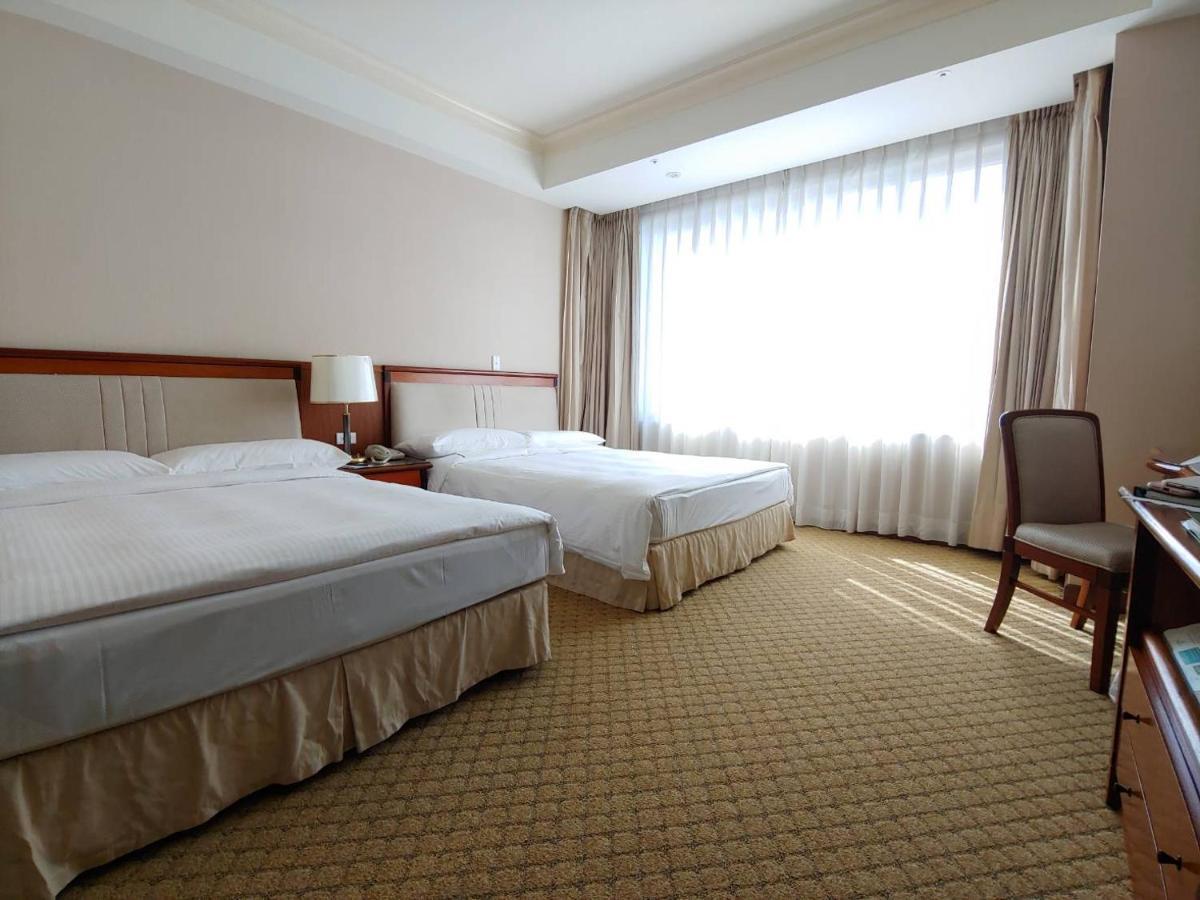 Evergreen Laurel Hotel - Taichung Luaran gambar The photo shows a neatly arranged hotel room featuring two beds: one double bed and one single bed. The room has beige walls and a warm color palette. Large windows with sheer curtains allow natural light to flood in, creating a bright and airy atmos