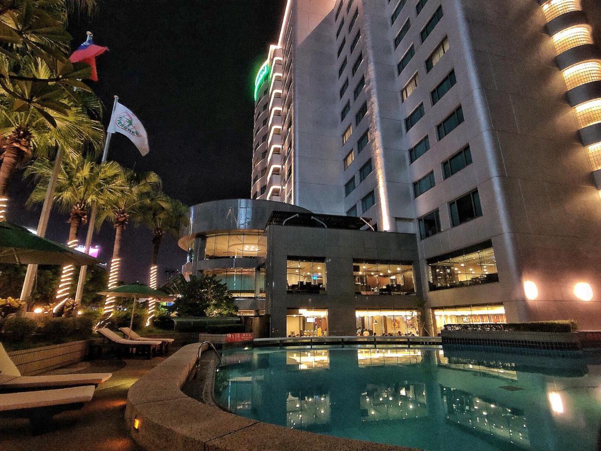 Evergreen Laurel Hotel - Taichung Luaran gambar The photo depicts a modern hotel or building at night, featuring a sleek facade illuminated by lights. In the foreground, there is a swimming pool that reflects the surrounding lights and palm trees. There are lounge chairs near the pool, and the atm
